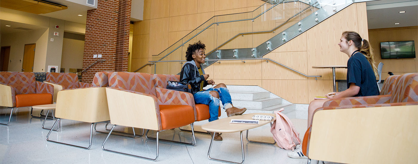 Two students sit and have a conversation on the bottom floor of the Gira Center