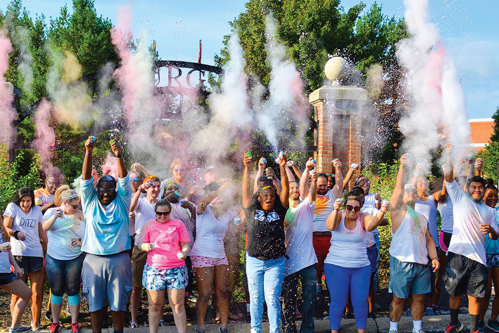 A large group of Greek Life students throw multi-colored dust into the air