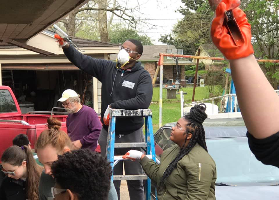 group of students volunteering by painting a house